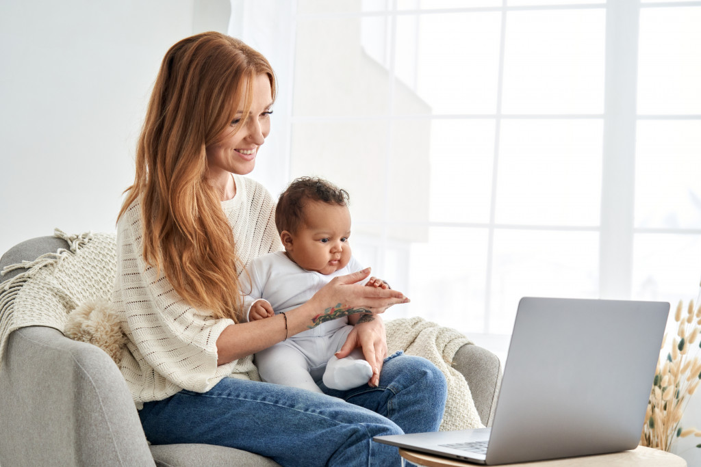 happy mom holding her baby while working in front of laptop