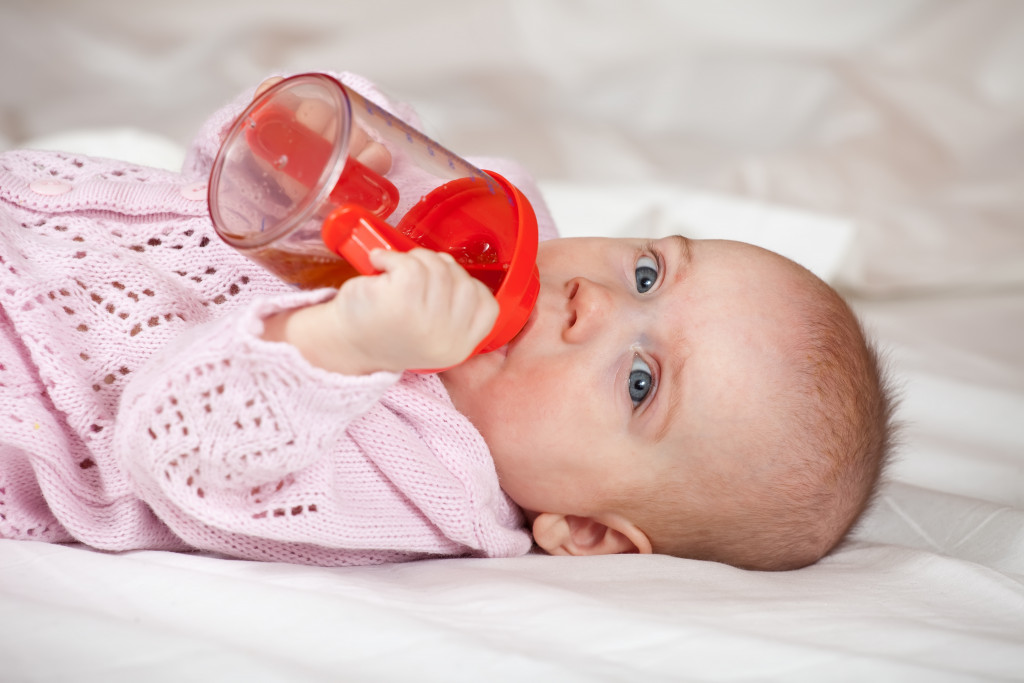 baby with sippy cup on a white blanket