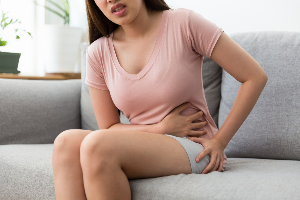 woman holding her tummy due to period cramps in living room couch